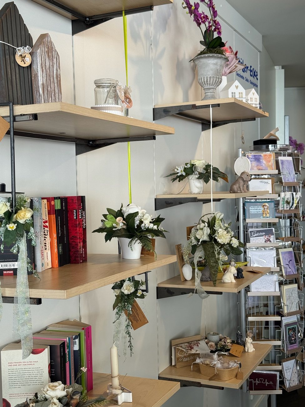 Regalwand im Lädchen des NENNA mit Blumen, Büchern und Grußkarten